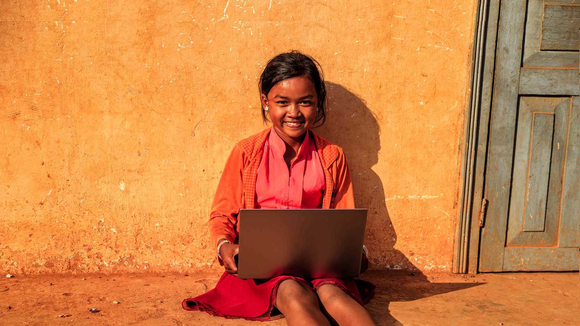 Expo Live - Cambodian girl sitting against a wall using a laptop