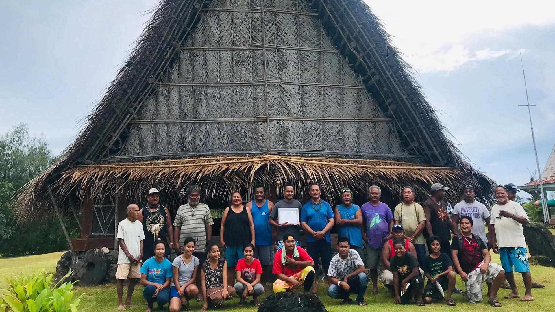 A group photograph of people from Micronesia standing in front of a hut